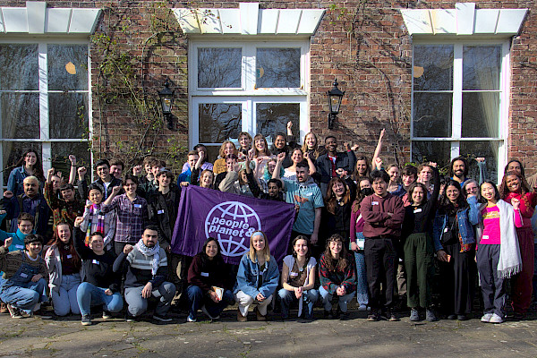 Large group of students with people & planet flag raising their arms and smiling in front of a building
