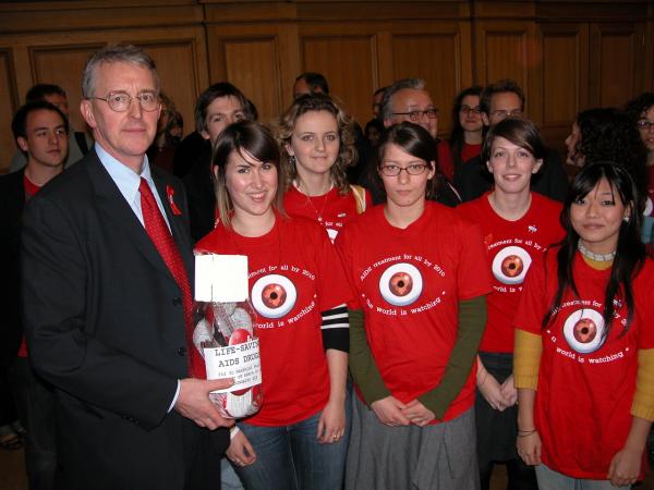 Photo of LSE People & Planet handing over a giant pill bottle filled with signed Treat AIDS Now action-cards to Hilary Benn