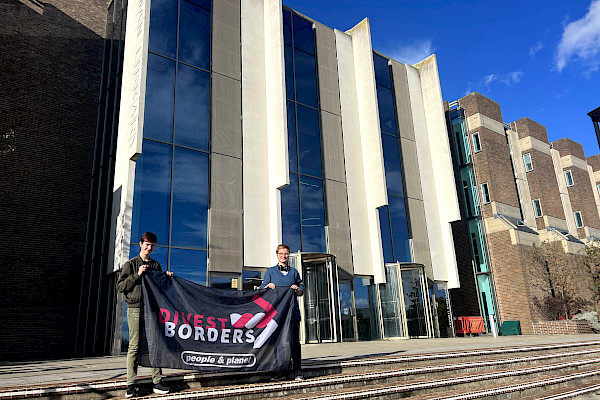 Two students stand with Divest Borders banner in front of university