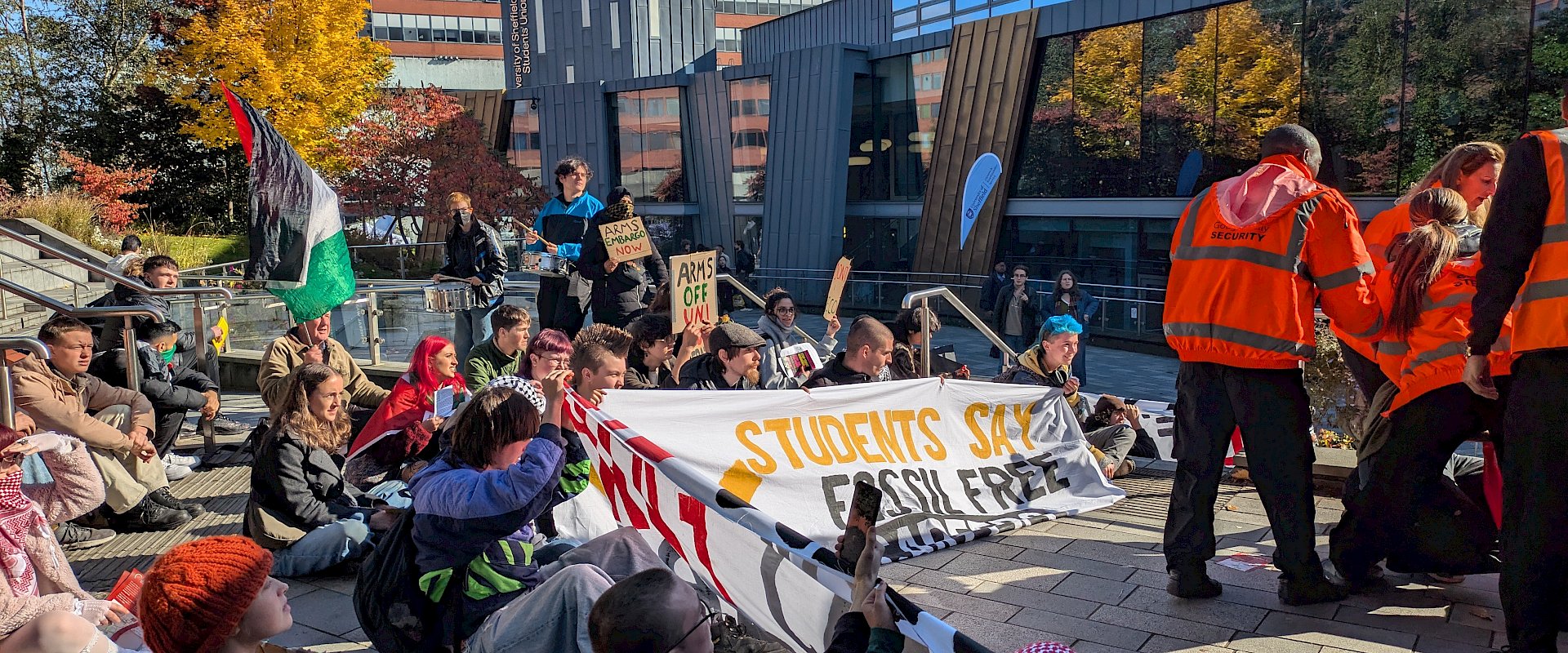 Large group of students at Sheffield University sit down obstructing the entrance of the university careers fair holding up banners which say Fossil Free Careers