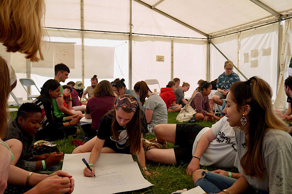 Students sitting in groups on grass in large marquee writing on flip chart paper